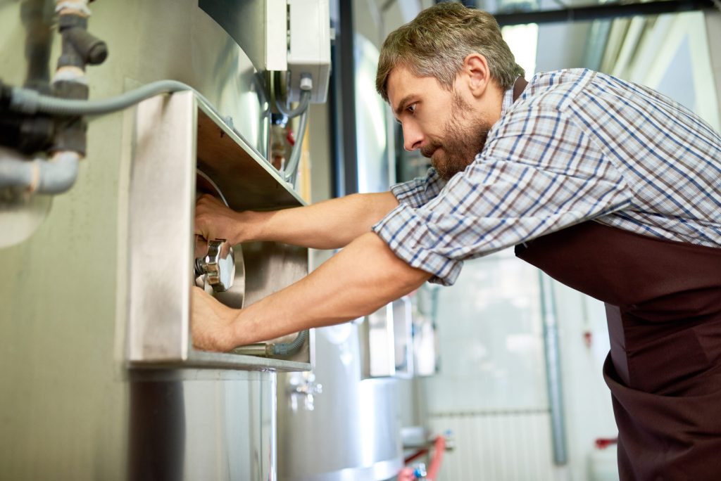 Busy skilled maintenance technician repairing brewery equipment