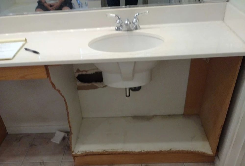 Bathroom vanity with sink; countertop intact, cabinet base removed exposing plumbing and a wall opening.