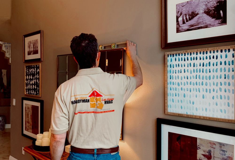 Man in a white Champion shirt with logo on the back, standing in a hallway with framed photos on the wall.